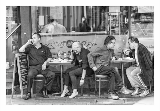 Four people sitting at a tables outside a cafe, engaged in conversation, two people on mobile phones, to people tlking to each other, black and white café print in minimalist living room, everyday people at outdoor bistro table, moody street photography, 