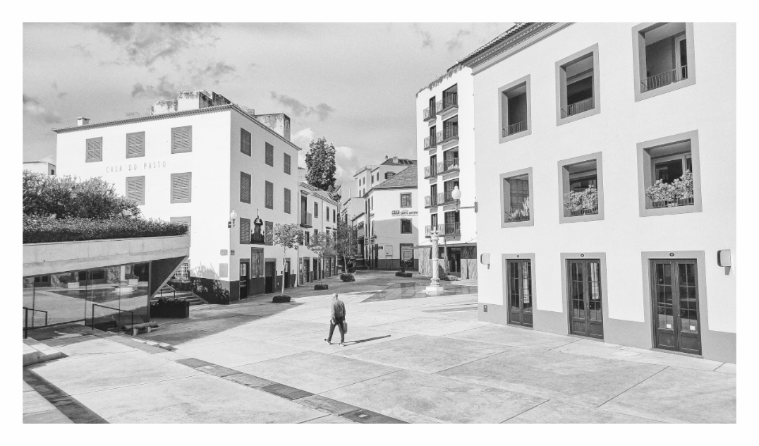 Black and white photo of a residential area with buildings and a person walking,Monochrome fine art photo showing a lone figure dwarfed by the grand architecture of a European piazza.