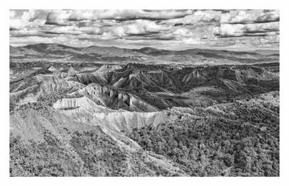 Black and white landscape of a canyon with mountains in the distance. Black and white fine art landscape photo of the Valle dei Calanchi (Valley of Badlands) in Italy, showcasing the deeply eroded, stark geological formations.