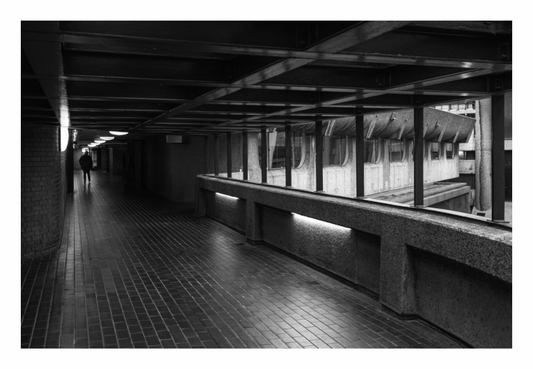 Long, narrow hallway with a reflective floor and glass walls, black and white urban tunnel print in minimalist living room, dimly lit concrete walkway on gray wall, moody street photography, modern beige sofa decor, Scandinavian interior styling