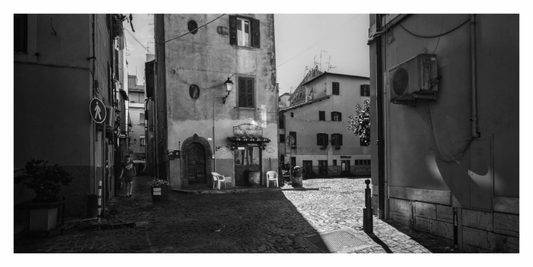 Black and white street scene with buildings and a cobbled square, Monochrome architectural print capturing a deserted, sun-drenched, narrow alley in an Italian town.