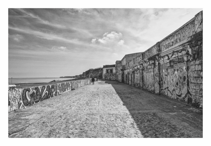 Black and white image of a coastal fort with graffiti on walls, black and white seawall beach print in minimalist living room, weathered stone path curving to horizon on gray wall, moody coastal landscape photography
