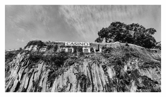 Casino building on a cliff with trees in the background. Black and white photo of an abandoned Casino building on a cliff overlooking the harbor in Madeira, emphasizing architectural decay and isolation.