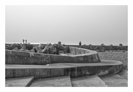 Black and white photograph of a coastal defense structure with people in the distance. Black and white architectural photograph of concrete steps in Madeira, with minimalist style emphasizing strong shadows and geometric lines.