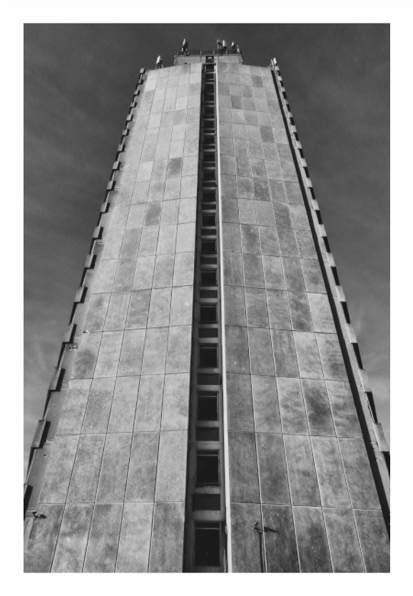 Tall concrete tower with a narrow vertical opening against a clear sky, black and white high-rise print in minimalist living room, towering concrete facade on gray wall, moody urban architecture photography