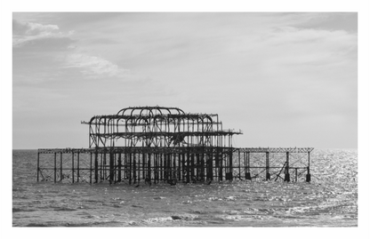 Black and white photograph of an old pier structure in the middle of a body of water, Dramatic monochrome print capturing the iconic, derelict West Pier silhouette against the water.