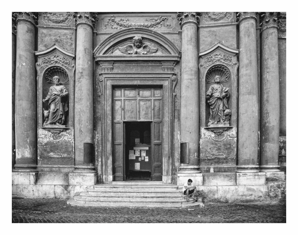 Black and white photo of a classical building entrance with statues and a person sitting on steps. Black and white fine art photo of a young man sitting on the steps of a historic church in Trastevere, Rome, capturing a moment of rest.