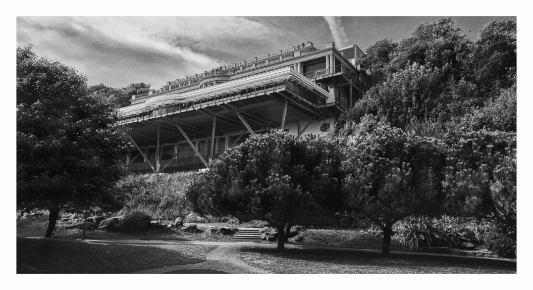 Monochrome photo showing the exterior facade and dramatic setting of the famous Leas Cliff Hall on the coast.