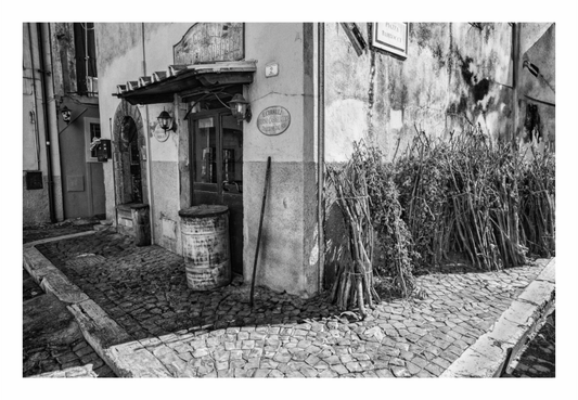 Black and white street scene with building entrance and barrels on a cobblestone street, Monochrome street photography print showing a historic stone-paved corner with European architecture in Italy.