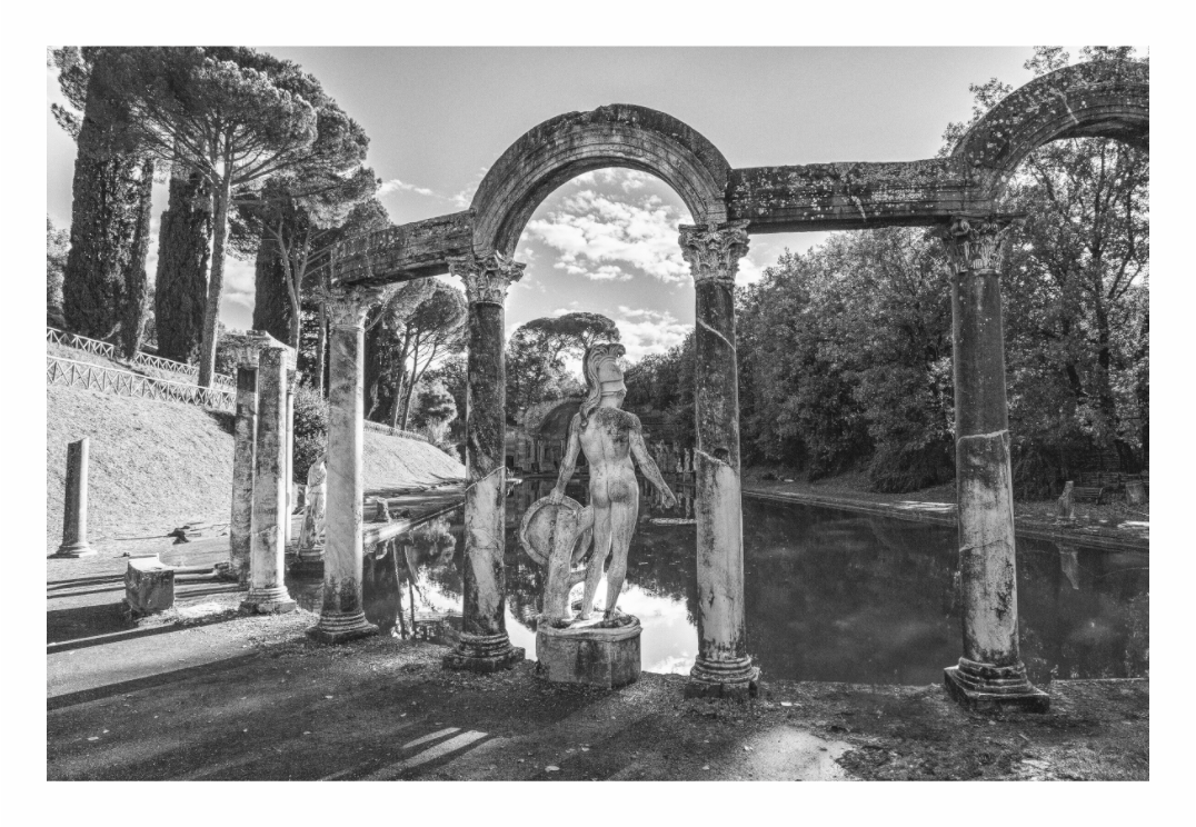Statue in a garden with classical architecture and trees. Black and white fine art photo of the ruins of Hadrian's Villa (Villa Adriana) near Tivoli, Italy, showcasing ancient Roman arches and architecture.